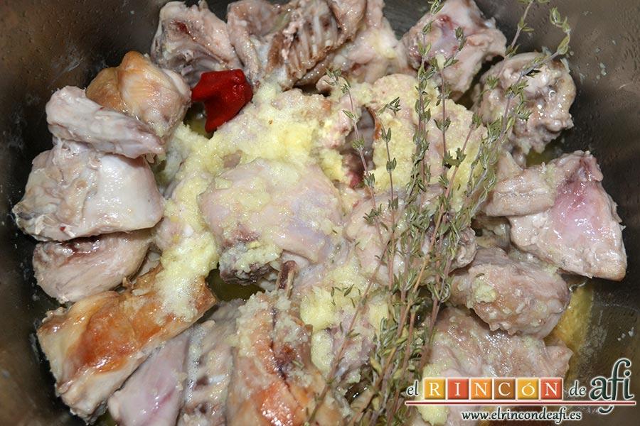 Conejo al ajillo, dejamos que vaya dorando y mientras trituramos bien los ajos pelados. Añadimos a la olla el ajo triturado, el trozo de guindilla, la pasta de caldo, el tomillo y el vasito de vino blanco