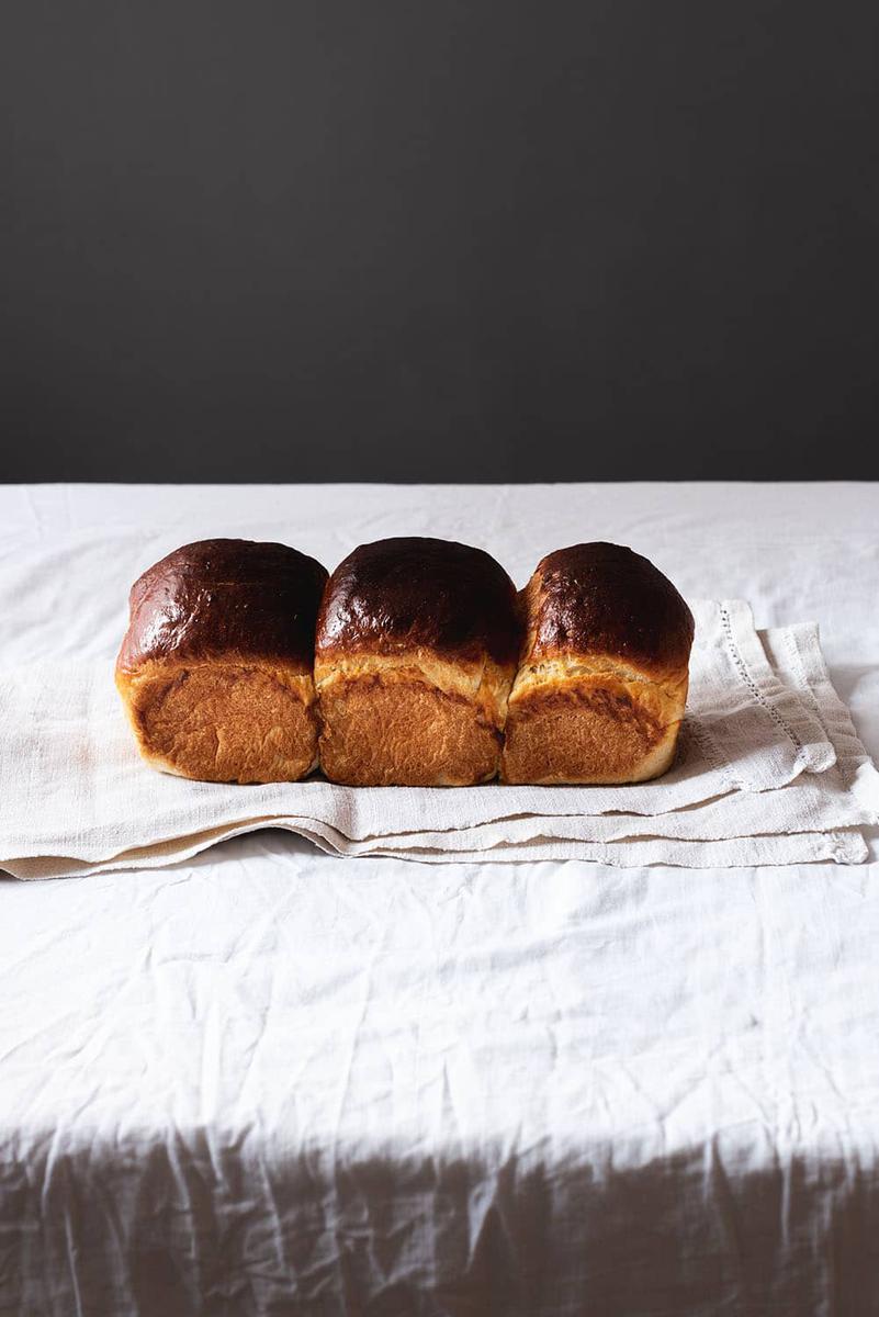 En una mesa está puesto un mantel blanco. Encima está el pan de brioche de la abuela entera.