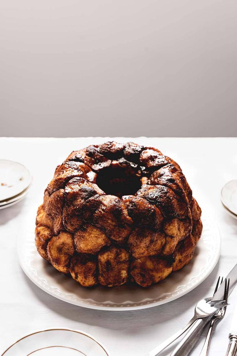 En una mesa, que está cubierta con un mantel blanco, está el Monkey bread. Alrededor hay platos blanco y cubiertos.