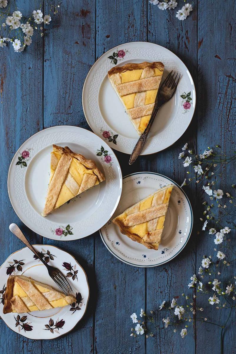 En una superficie azul están varios platos. En cada una hay una ración de crostata de ricotta. También hay unas flores blancas.