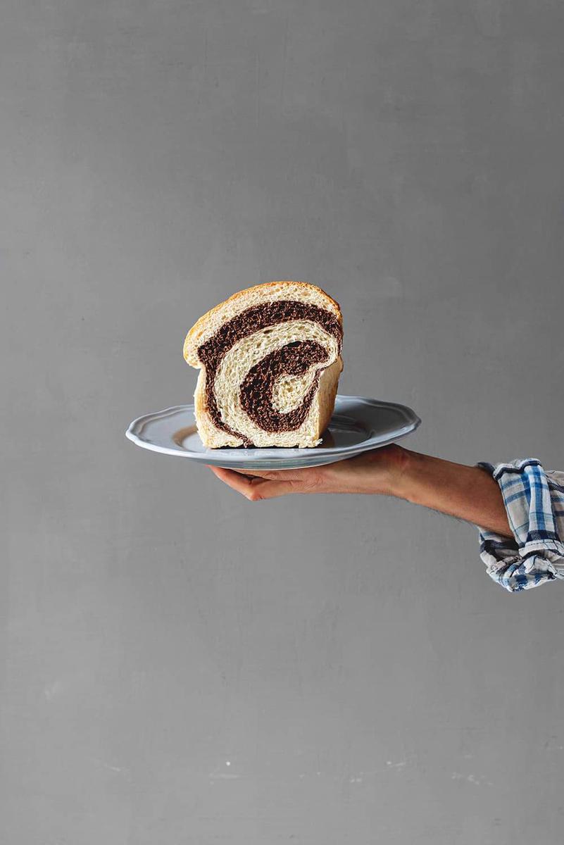 Delante de una pared gris una persona está sujetando un plato. En este plato está un trozo de pan de brioche marmolado cortado.