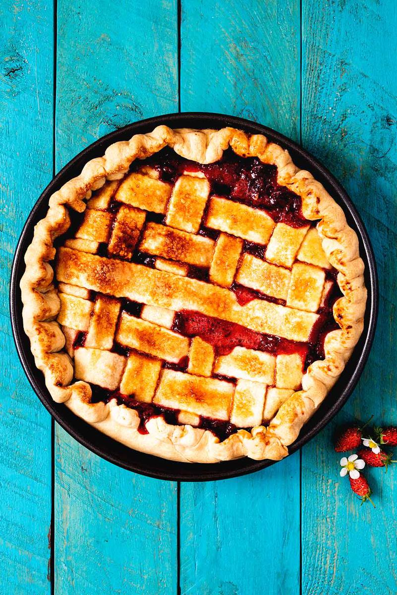 En una mesa azul está el pie de fresa. Al lado hay unas fresas frescas y flor de fresa.