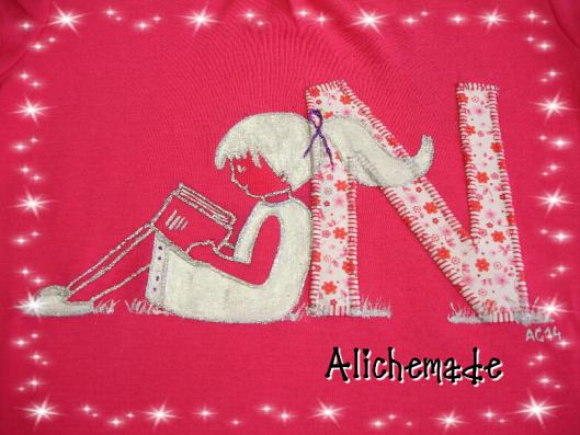 Detalle de la camiseta con inicial aplicada y niña leyendo pintada a mano.