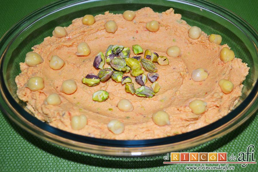 Hummus con pimientos y pistachos, colocamos la mezcla en un recipiente adecuado extendiéndola con una cuchara dejando unos círculos en la zona del medio y decorándolo con los garbanzos y los pistachos que teníamos reservados