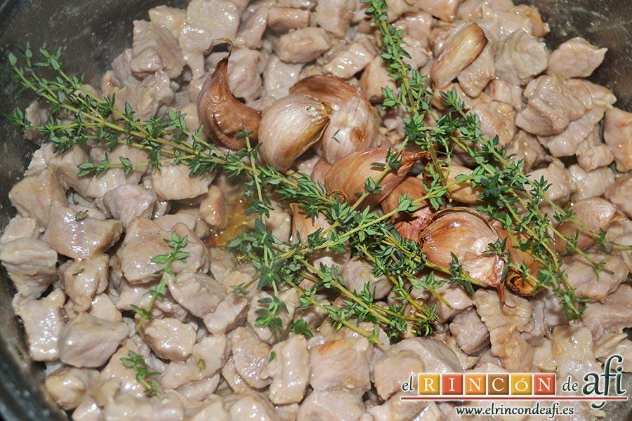 Cochifrito con papas brutas, cuando esté toda la carne bien frita le añadimos los dientes de ajo reservados con las ramas de tomillo fresco