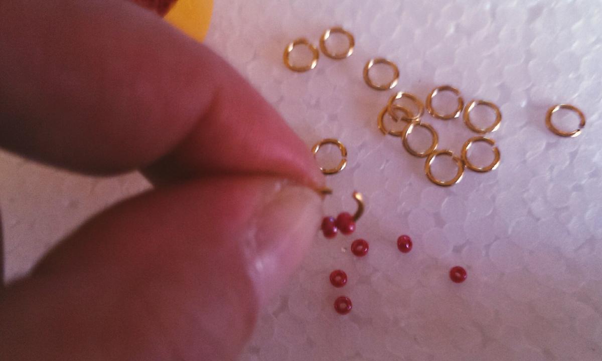 Abrimos nuestra anilla con un alicate pequeño, o ayudándonos de las tijeras. Metemos algunas cuentas.