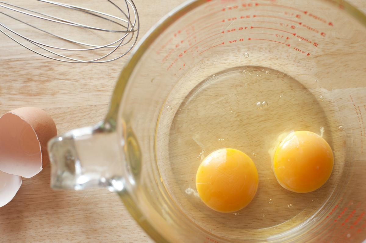 Overhead view of two healthy yellow egg yolks broken into the bottom of a clear glass measuring jug on a kitchen counter to be used as a breakfast or baking ingredient