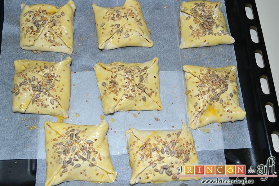 Pañuelos de hojaldre con jamón o pechuga, batimos bien el huevo y pintamos los pañuelos de hojaldre con el huevo usando un pincel de cocina. Espolvoreamos por encima las semillas de girasol y las semillas de sésamo