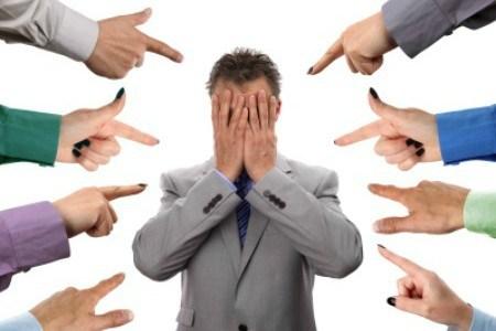 Hands pointing towards businessman holding head in hands concept for blame, accusations and bullying