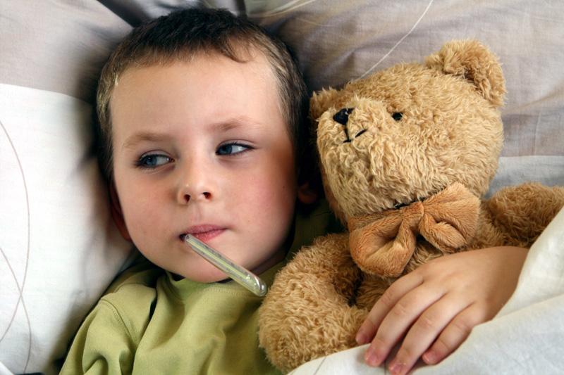 Young child with thermometer and sweet taddy lying in bed with flu and fever. Child with a temperature.