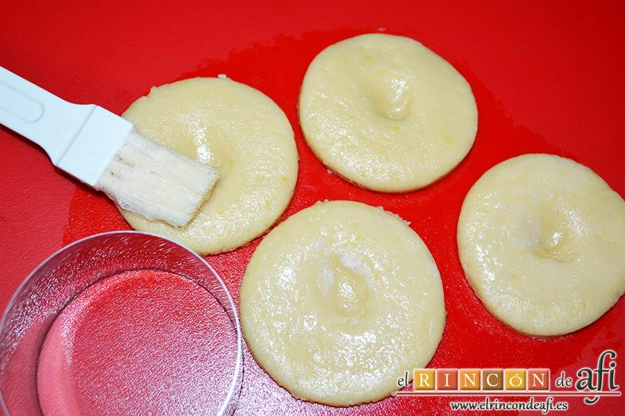 Perrunillas, hacer un hueco con el dedo en el centro de cada perrunilla y con un pincel de cocina pintar de clara espumada