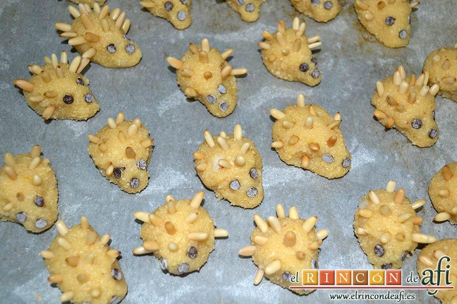 Erizos de panellets, dejar reposar la masa, formar ericitos sobre papel de horno, decorar con pepitas de chocolate y piñones