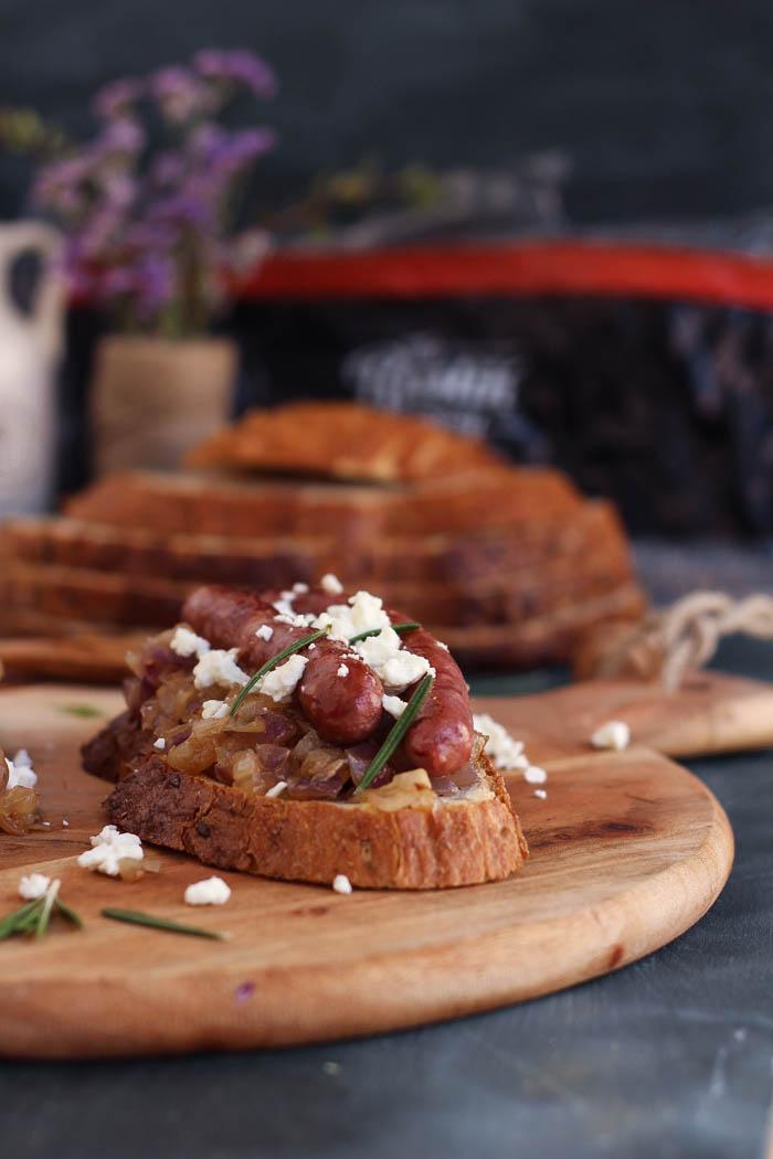 Tosta de salchichas, feta y cebolla caramelizada