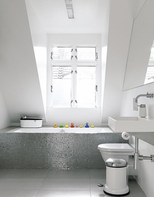 Un gresite plateado multiplica la luz que entra por la ventana, a la vez que añade interés a un espacio totalmente blanco brillante. Duravit y Corian son las firmas del sanitario y el lavabo respectivamente.