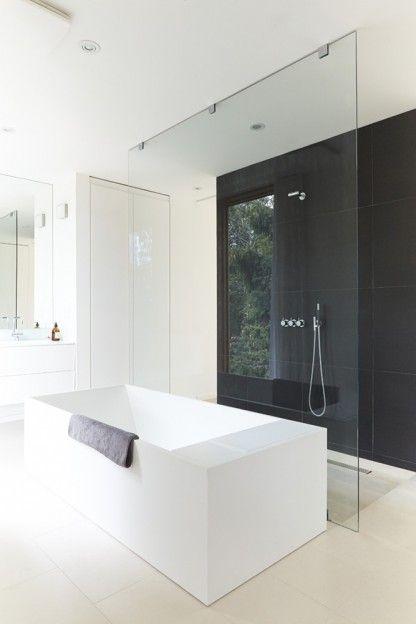 Baño minimalista en blanco y negro. La bañera queda centrada y sirve de apoyo a la mampara de la ducha