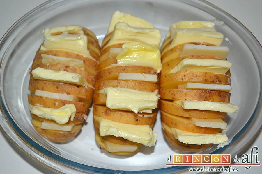 Papas al horno Hasselback, ponemos las papas en una fuente de horno e introducimos en los cortes queso y mantequilla de forma alterna