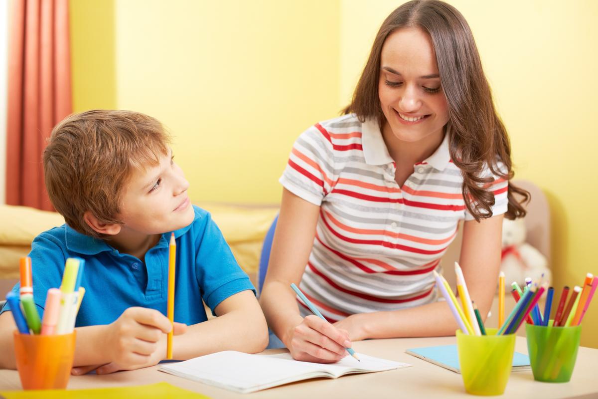 Portrait of cute schoolboy and his mother making schoolwork at home