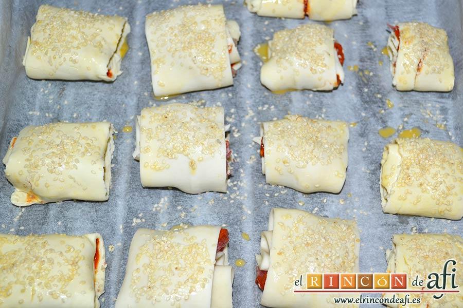 Rollitos de hojaldre rellenos de crema de pimientos y salchichas frescas, pintar los rollitos con huevo batido y espolvorear con semillas de sésamo, y hornear