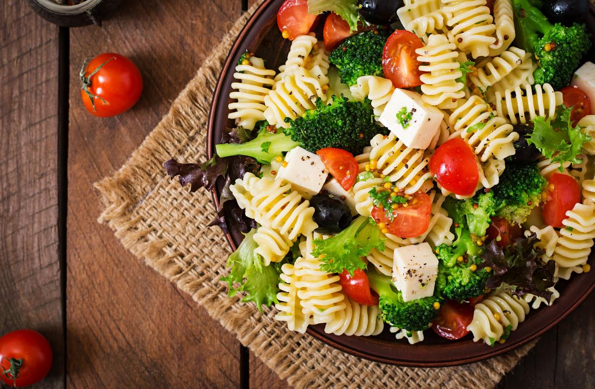 Pasta salad with tomato, broccoli, black olives, and cheese feta. Top view