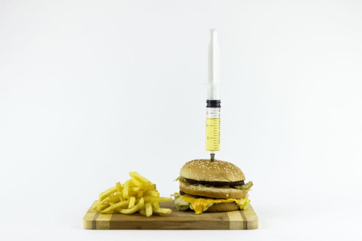 47772379 - syringe puming yellow liquid in a hamburger, on a white background