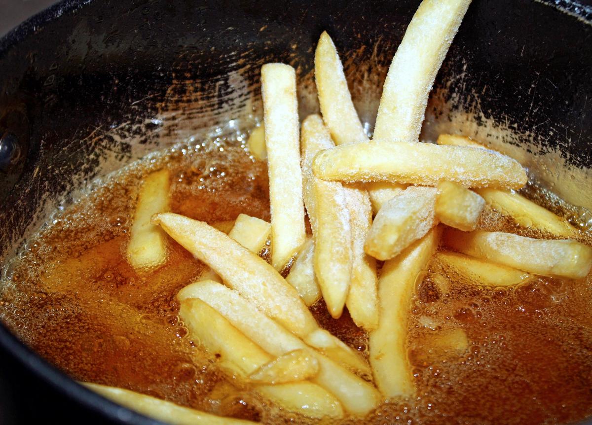 37562037 - frozen french fries going into a deep fryer filled with hot oil