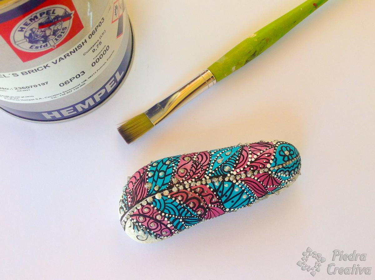 Manualidad de piedra con pluma pintada y barnizada