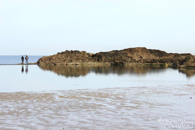 paisaje con dos personas al fondo y una montaña pequeña y agua