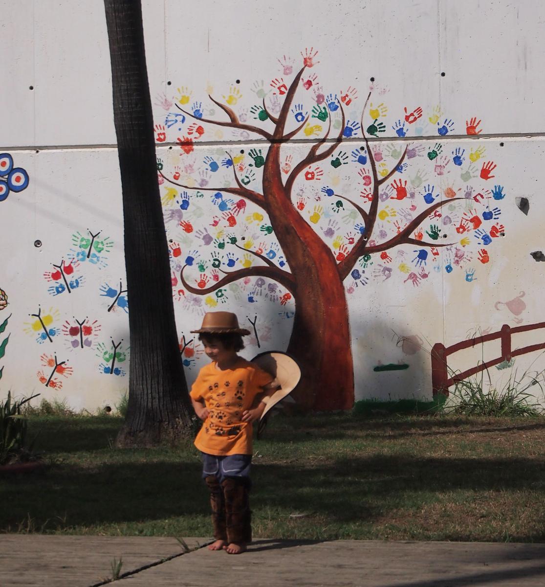 Niño disfrazado y grafiti con arbol de manos detrás 