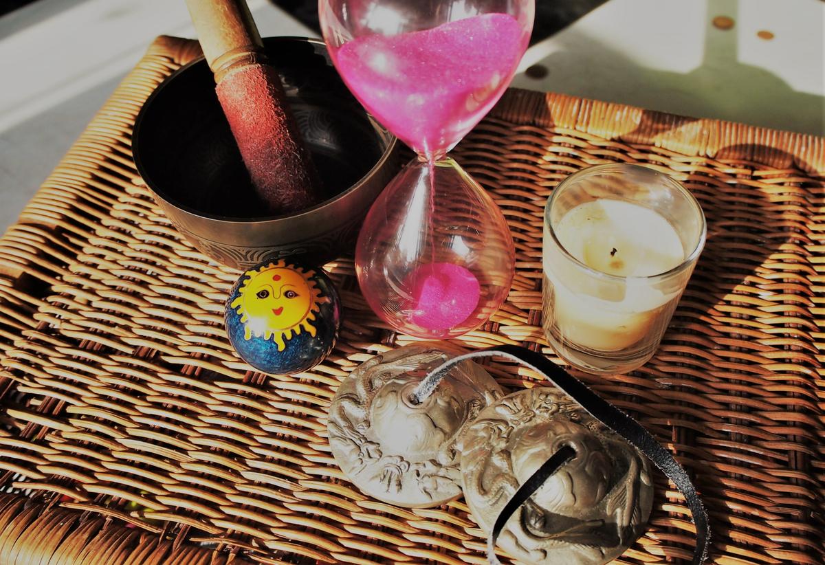 Bodegon de objetos: cuenco tibetano, reloj de arena, vela, platillos y bola de sonido
