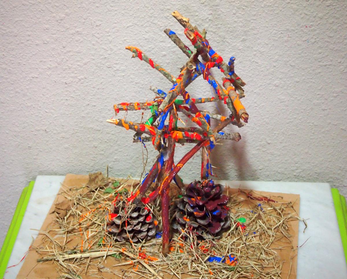 Resultado final. Palos pegados aleatoriamente, pintados con tempera y con una base de paja y piñas. Animalitos entre la paja