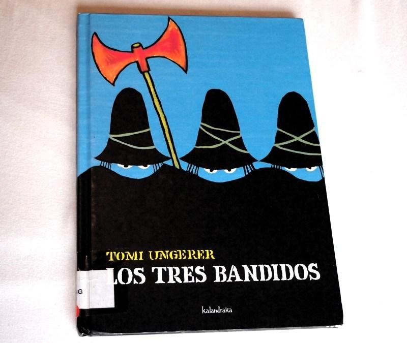 Portada de: Los tres bandidos. Fondo azul y siluetas de bandidos con corro y hacha