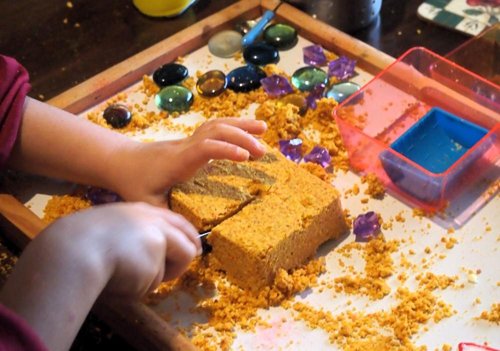Manos de niños cortando una tarta hecha de arena magica de madarina