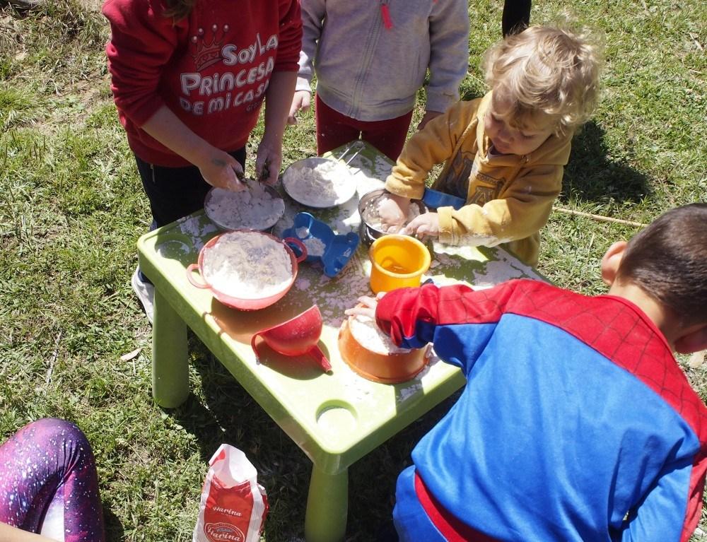 Niños jugando con la harina y cacharritos en una mesa en el parque