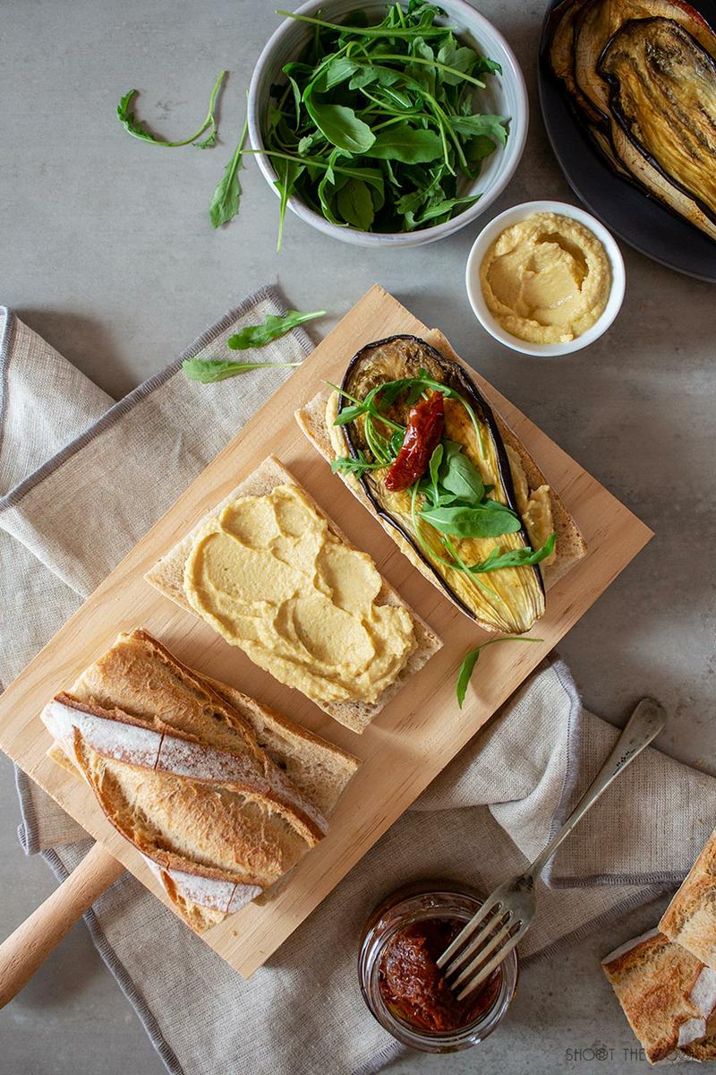Bocadillos saludables de hummus, berenjena, tomate seco y rúcula