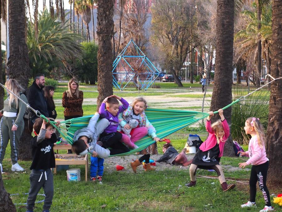 Niños y niñas jugando en una hamaca. Familias observando de fondo, una de las normas del grupo de juego es acompañar y cuidar