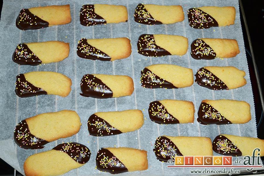 Lenguas de gato de naranja, decorar las lenguas mojando una parte en el chocolate y espolvorear con las bolitas