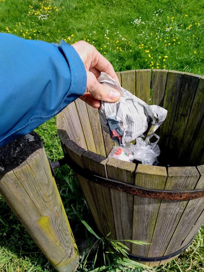 Tirando la caca de perro a la papelera usando papel de periódico.
