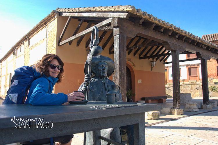 Peregrina sentada en una mesa con una estatua del Camino de Santiago