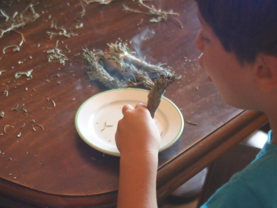 Un niño soplando un atillo de aromáticas secas prendidas para un sahumerio, humo alrededor