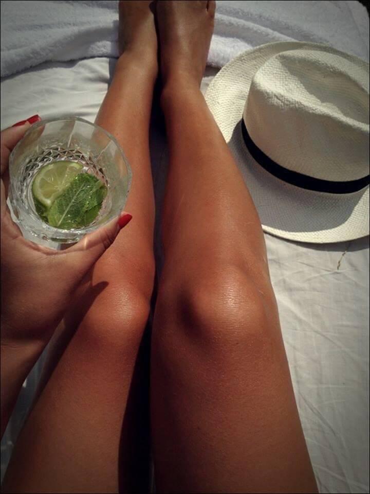 piernas de mujer tomando el sol con sombrero y mojito