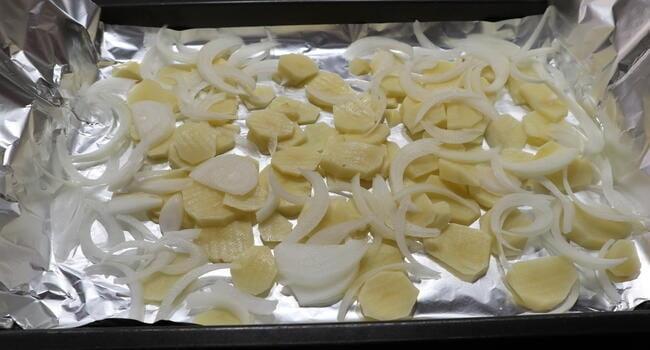 Ponemos la bandeja con el papel albal y le colocamos la patatas en rodajas y la cebolla cortada en láminas