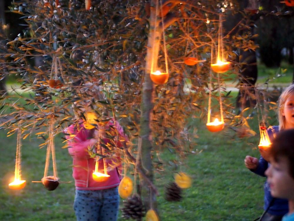 Ninos y niñas mirando velas alrededor de un árbol de navidad decorado en un parque
