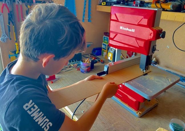 Niño cortando una madera en un taller con maquinaria