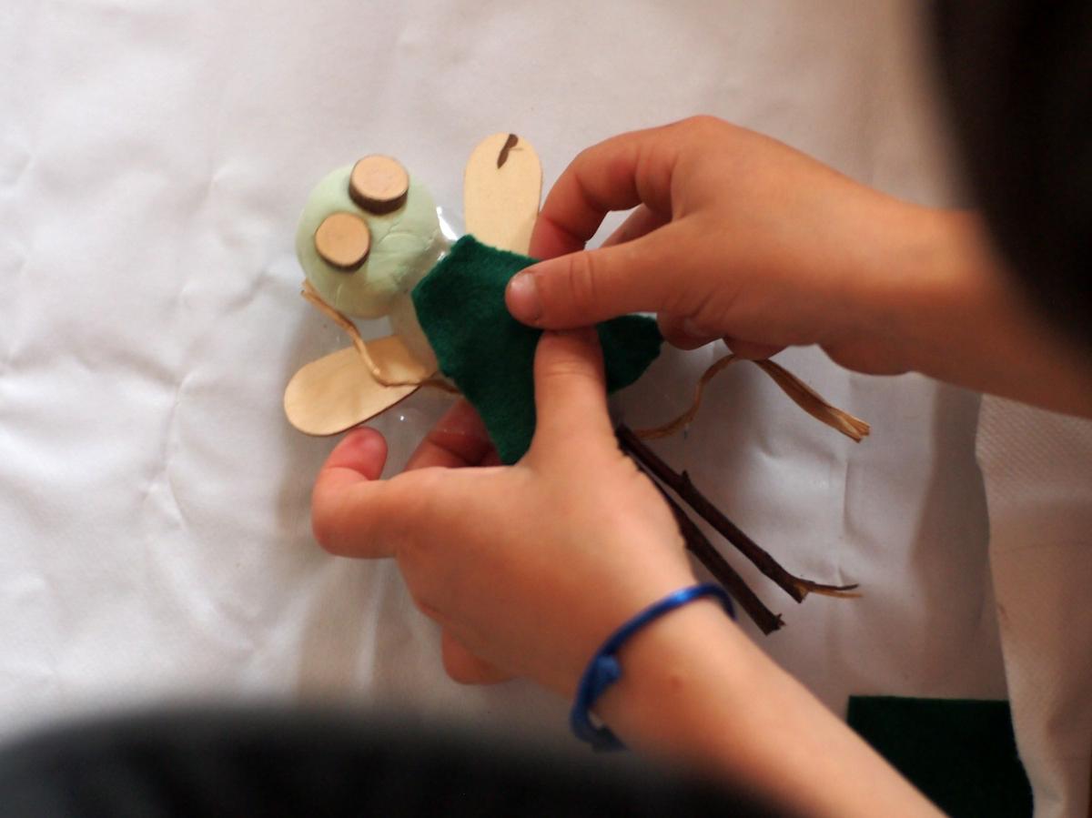 Manos de niño poniendo tela encima de una hada hecha de pasta de modelar y elemetos naturales