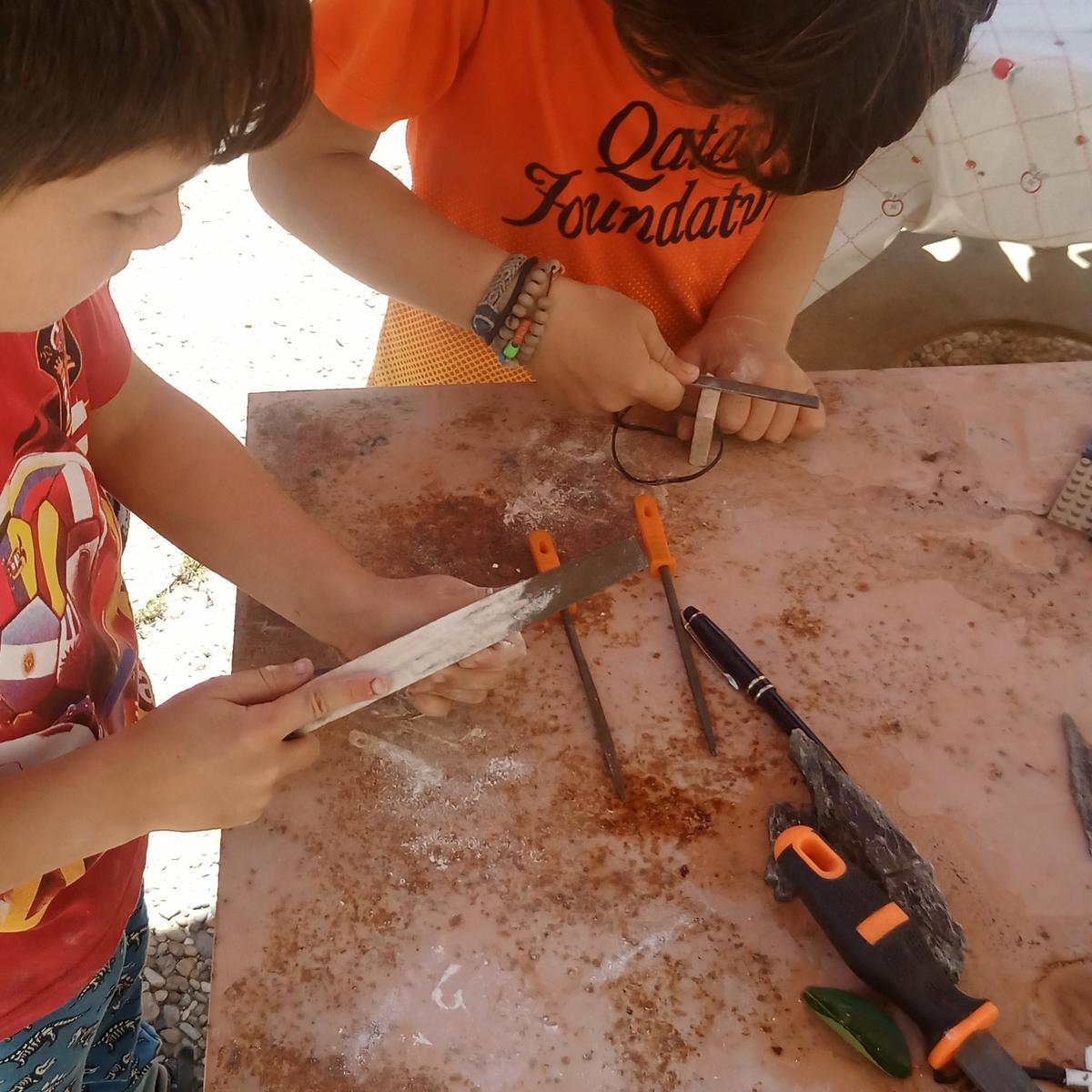 Niños en una mesa con herramientas tallando piedra blanda, material del método de Naturaleza Creativa