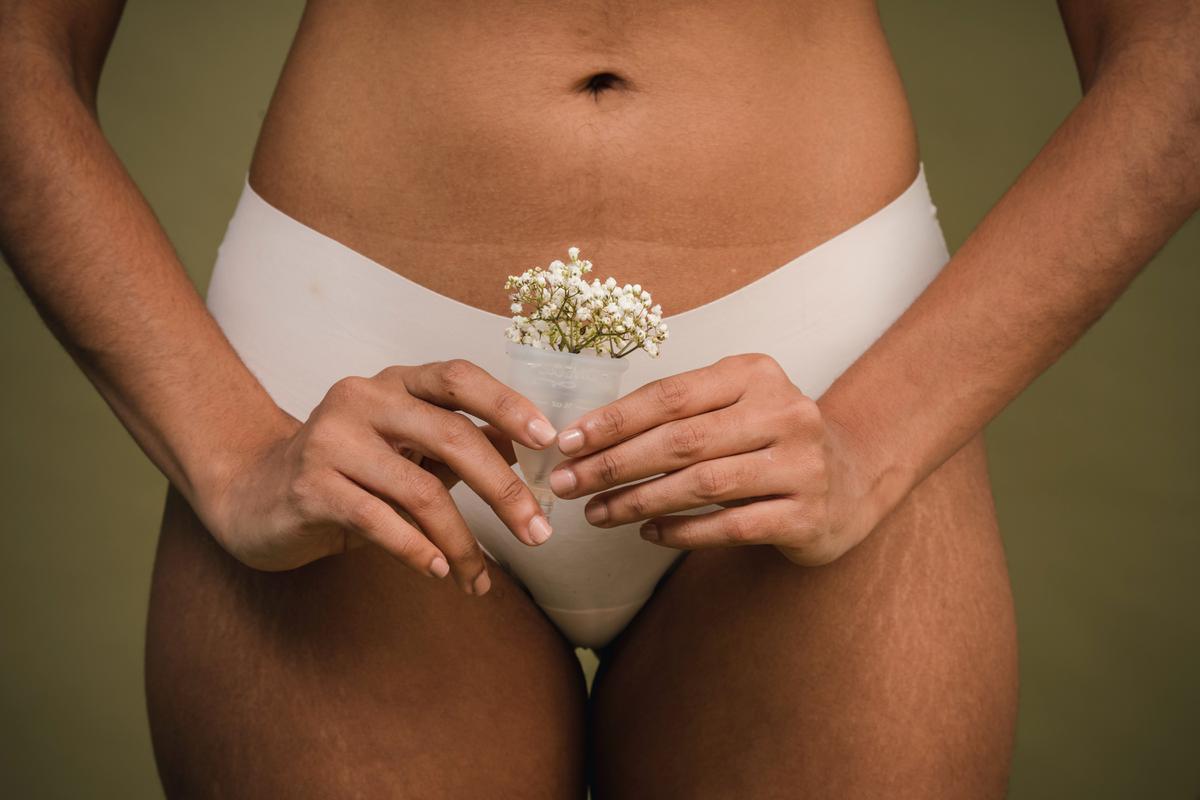 Mujer en bragas con una copa menstral llena de flores en frente de su abdomen