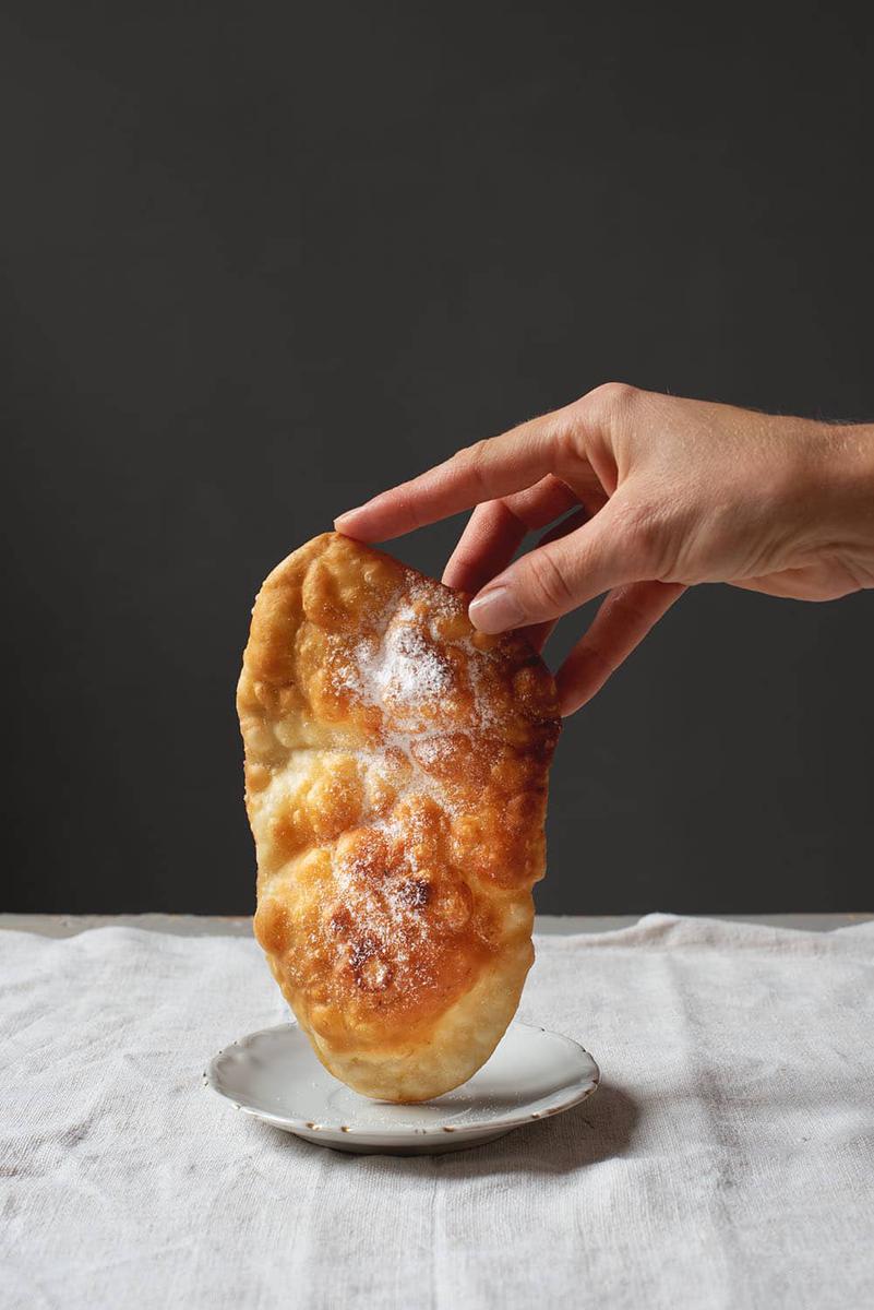 Una mano sujeta una oreja Carnaval fina y crujiente encima de un plato.