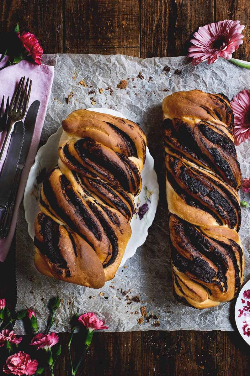 En una mesa de madera está puesto un papel de horno. Encima están las dos babkas . Se ven que están rellenos con chocolate.