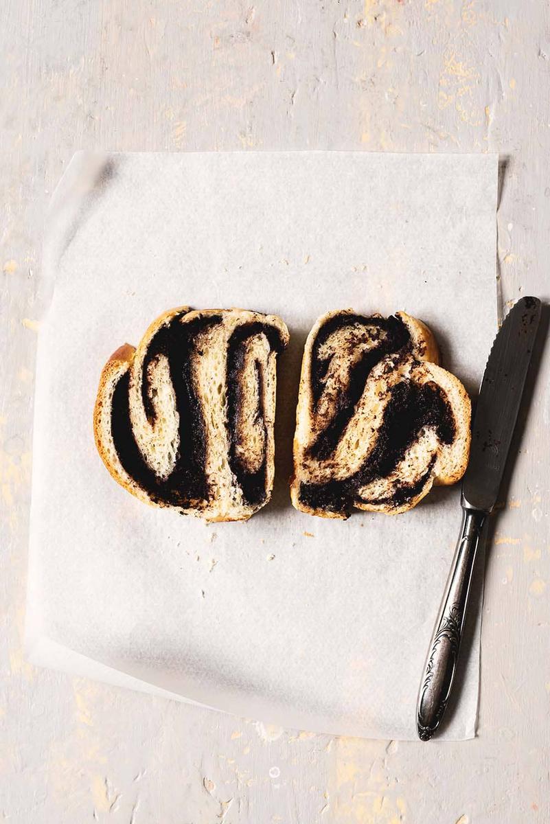 En la mesa gris está puesto un trozo de papel de horno. Encima están dos rodajas de babka de chocolate.