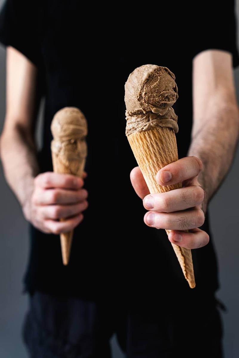 En la mano, de un chico vestido en una camisa negra, hay dos cucuruchos. Te ofrece uno de los dos para comerlo.